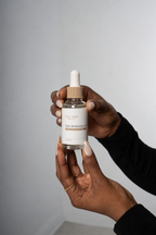 LoccBar Essentials Root Stimulating Oil held in manicured hands against a soft gray background