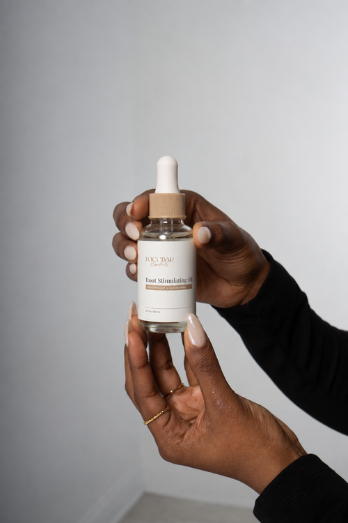 LoccBar Essentials Root Stimulating Oil held in manicured hands against a soft gray background
