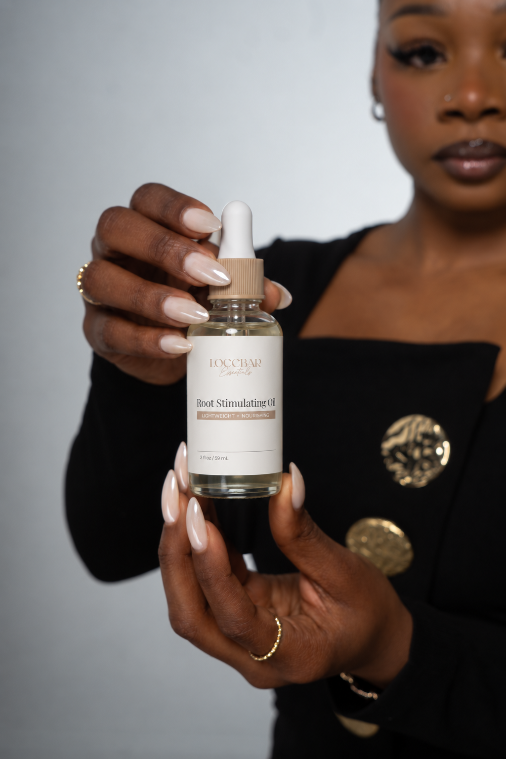 Marquesta holding LoccBar Essentials Root Stimulating Oil against a soft gray background
